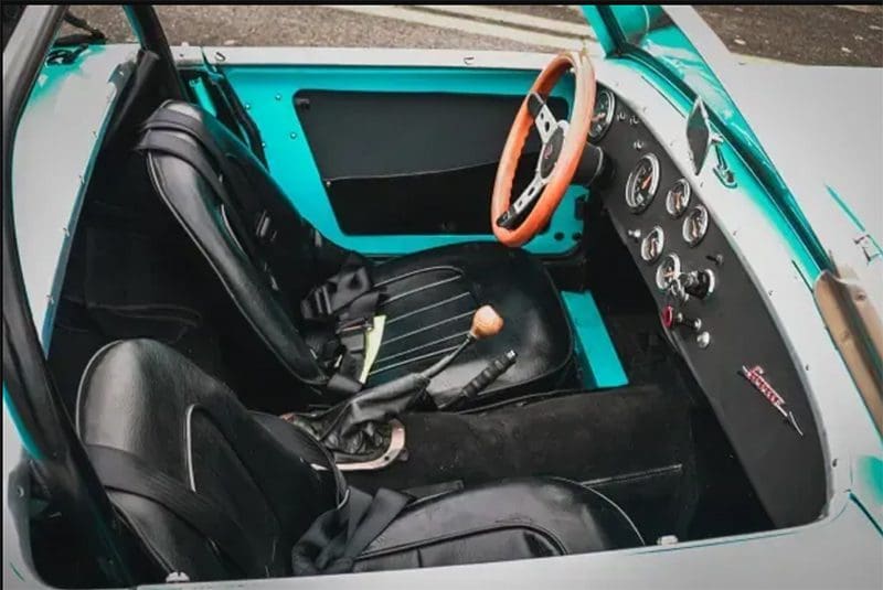 Interior of a classic car with black seats and wooden steering wheel.