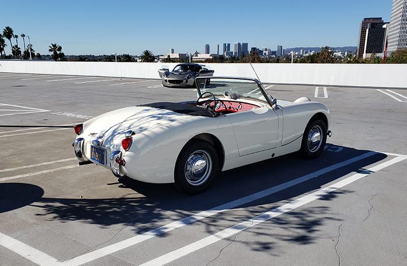 Classic white convertible car parked on a rooftop with city skyline in background.