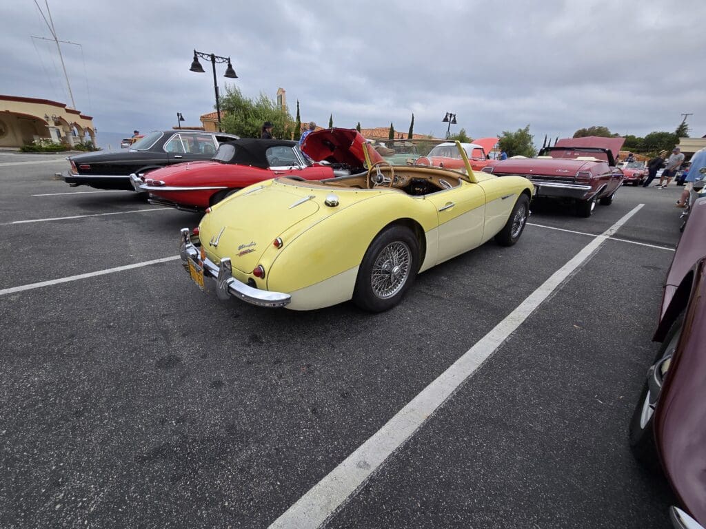 A yellow vintage convertible car parked among other classic cars.