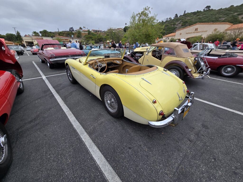 Yellow classic convertible car parked among vintage vehicles.