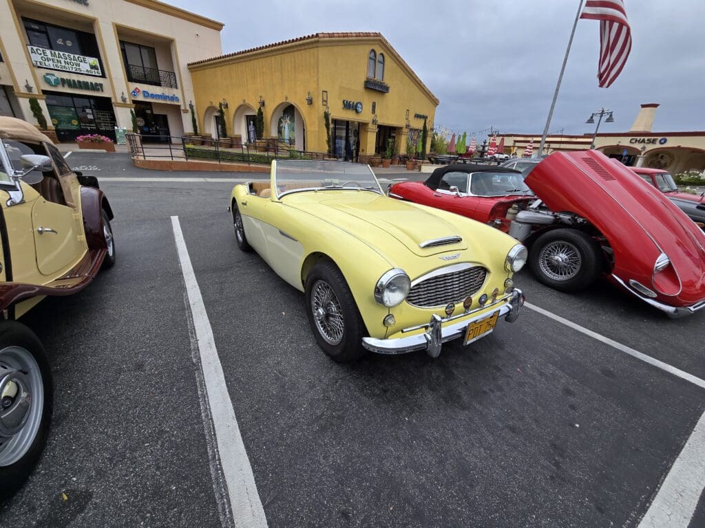 Classic yellow convertible car parked in a lot near shops.