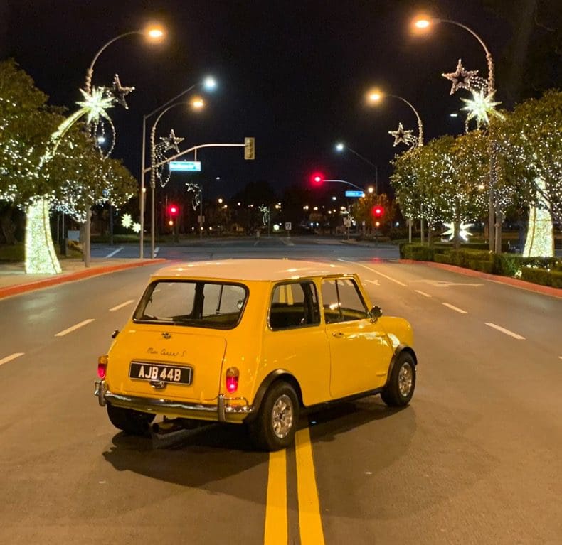 Yellow vintage car parked on an empty, decorated street at night.