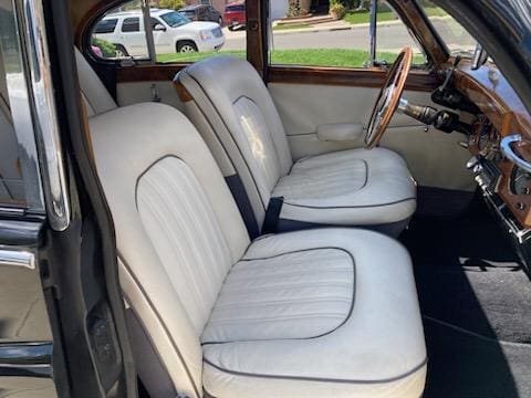 Classic car interior with white leather seats and wooden steering wheel.