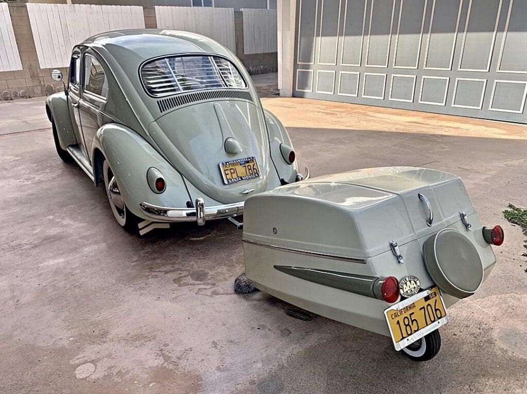 Retro Volkswagen Beetle with a unique vintage trailer attached in a garage.