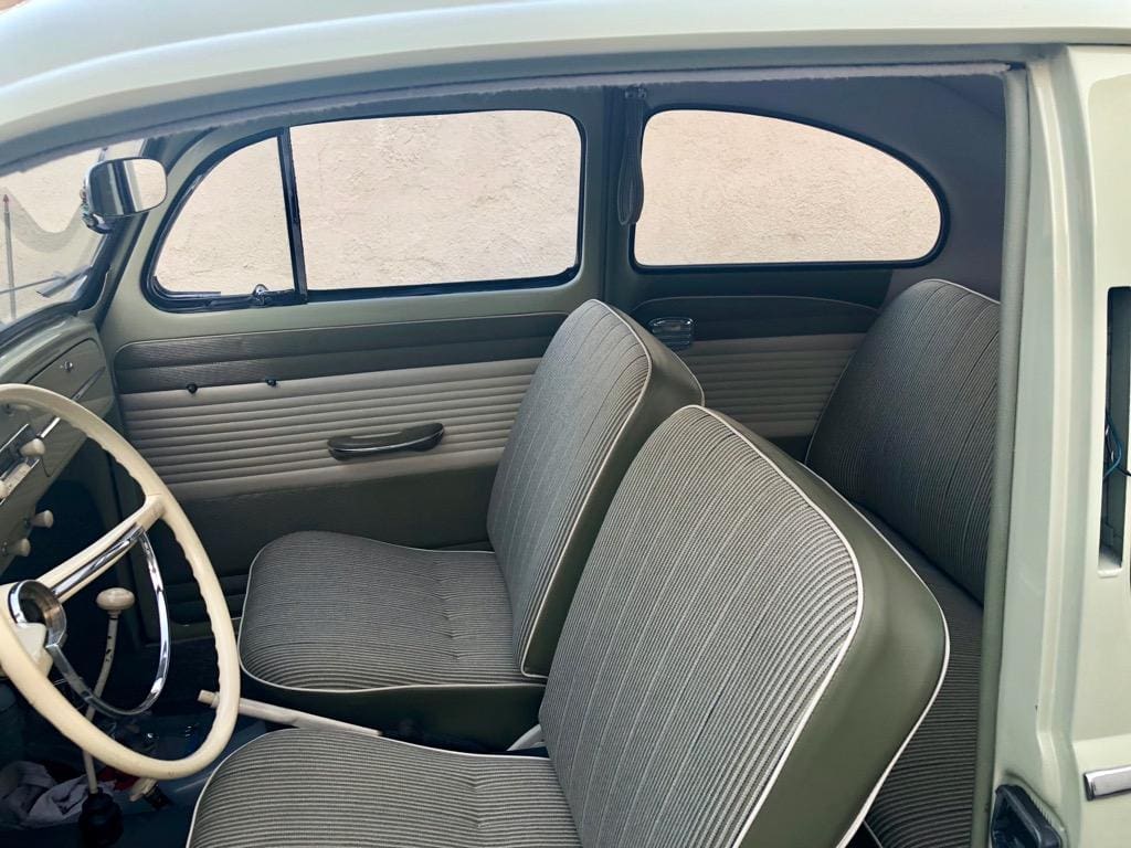 Interior view of a vintage car with simple gray seats and a white steering wheel.