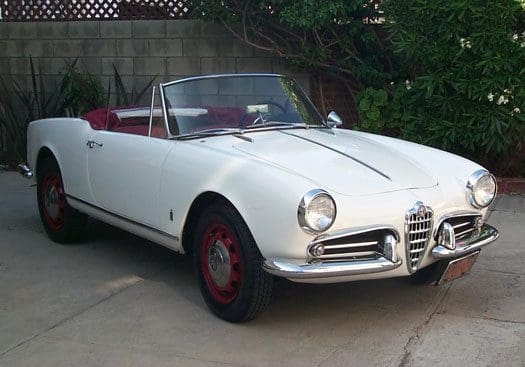 Classic white convertible car with red wheels parked outdoors.