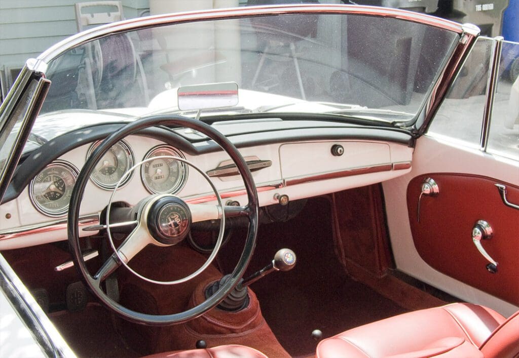 Vintage car interior with classic steering wheel and red leather seats.