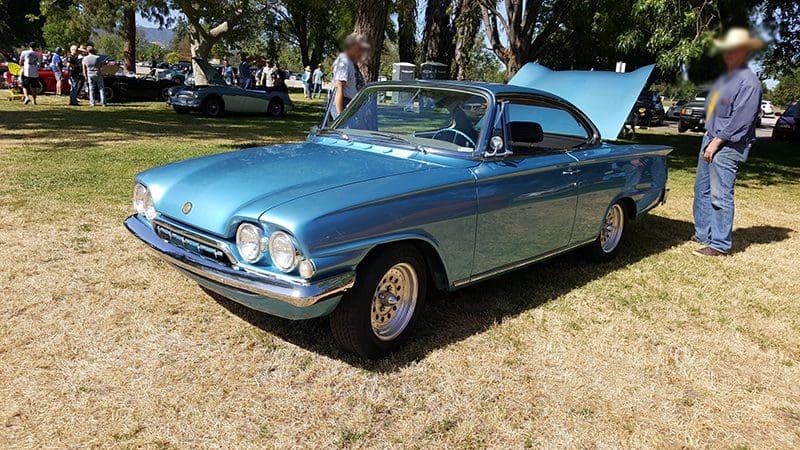 Classic blue vintage car parked on grass at an outdoor event.
