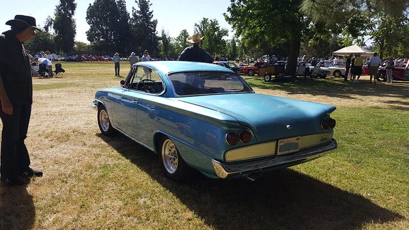 Classic blue vintage car parked on grass at a sunny outdoor event.