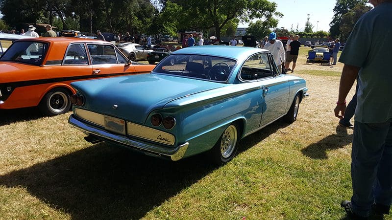 A classic blue vintage car parked on grass at a sunny outdoor event.
