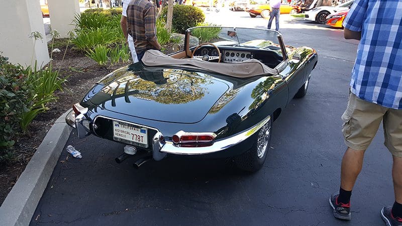 A shiny black vintage convertible car parked outdoors on a sunny day.