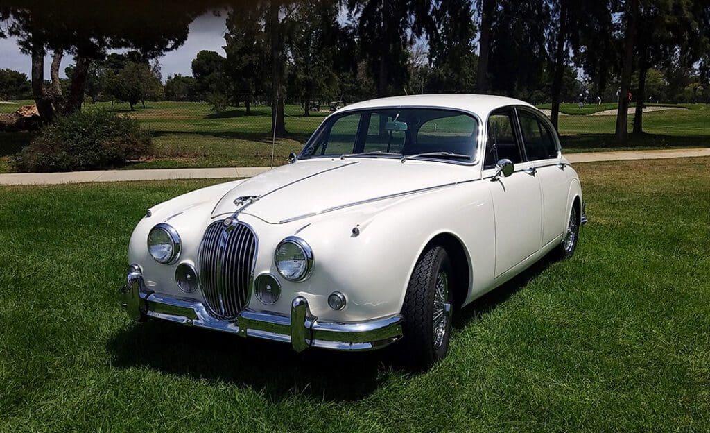 Classic white vintage car parked on grass under trees.