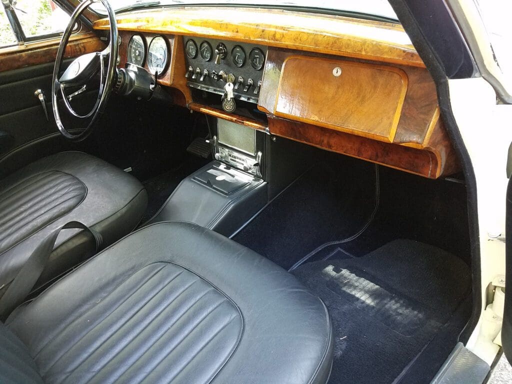 Classic car interior with wood dashboard and black leather seats.