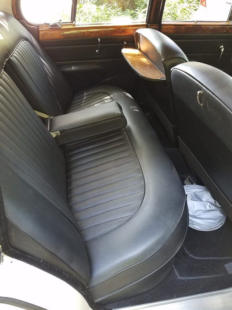 Black leather backseat of a car with a white bag on the floor.
