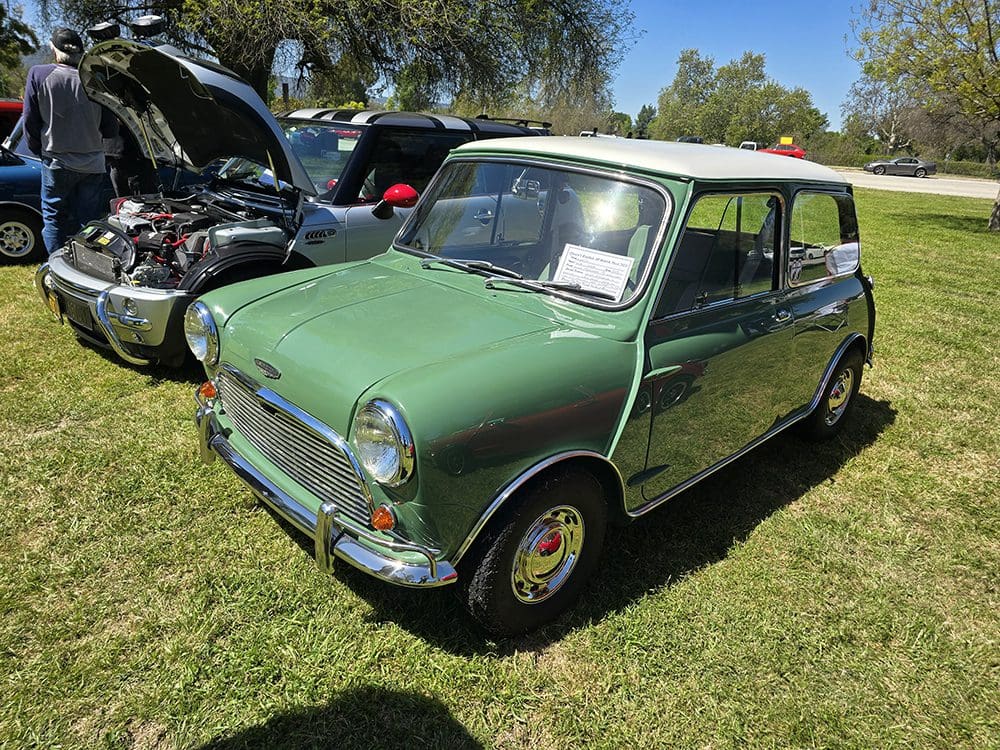 Classic green vintage Mini Cooper parked on grass at car show.