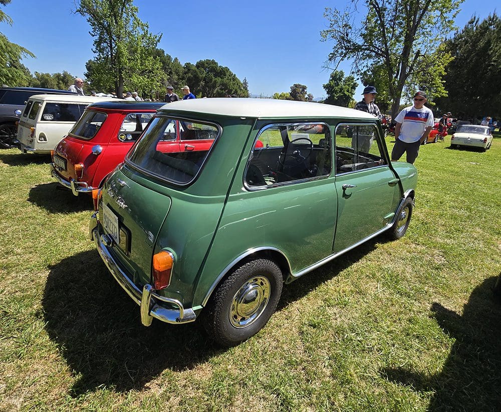 Classic green Mini Cooper with a white roof parked on grass.