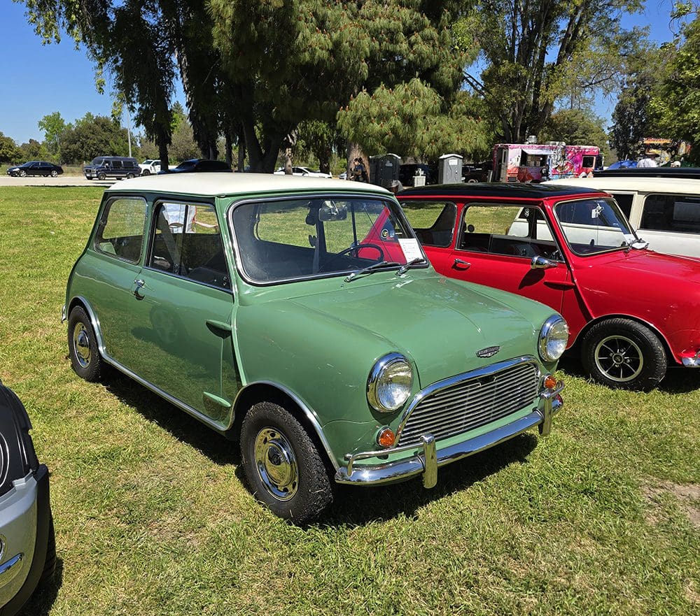 Classic green Mini Cooper parked on grass at a sunny outdoor event.