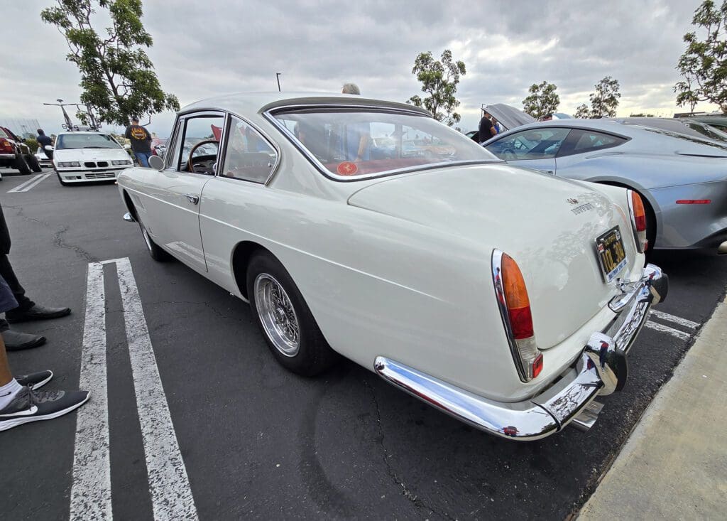 White classic car parked in a lot under cloudy sky.