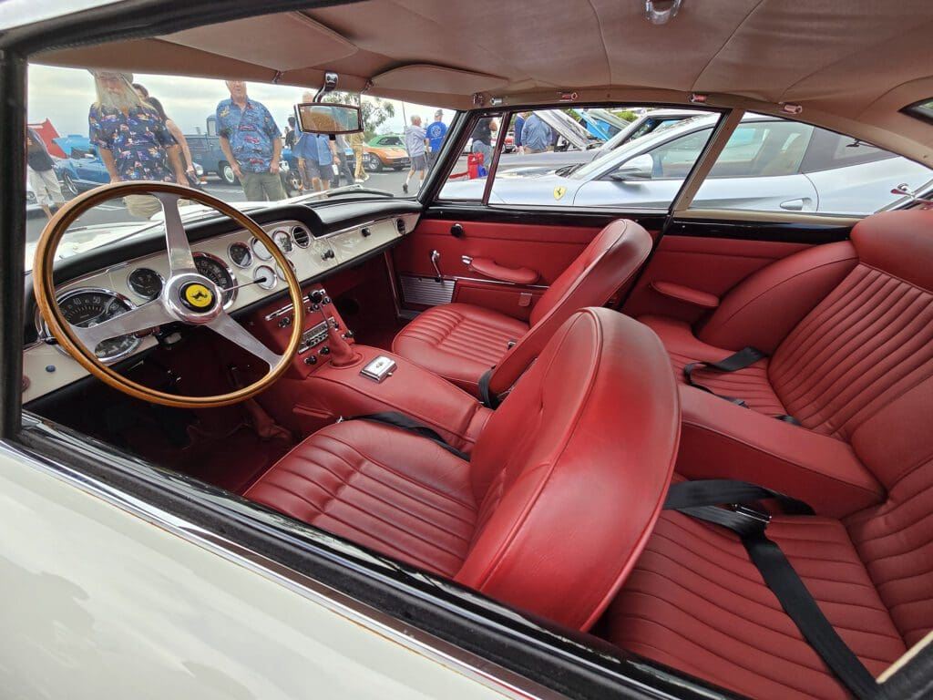 Classic car interior with red leather seats and wooden steering wheel.