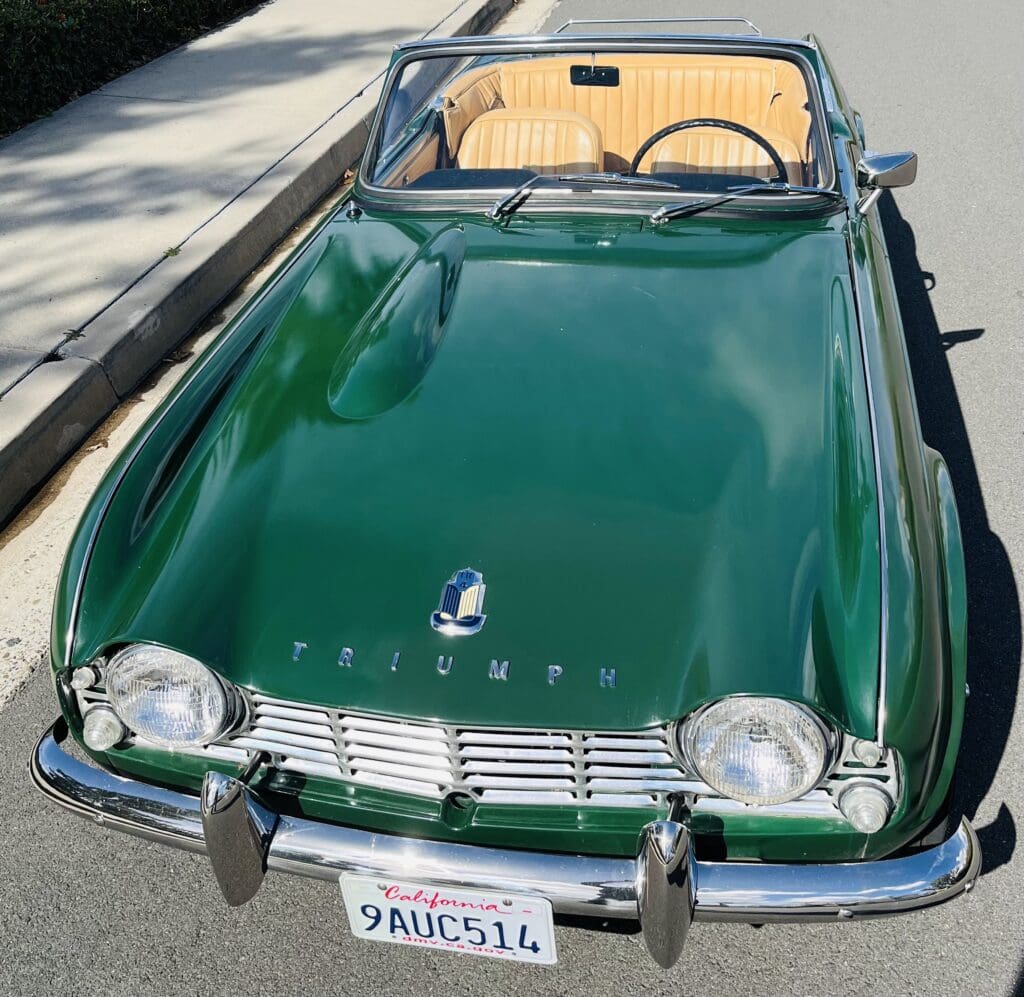 Classic green convertible car parked on a sunny street.