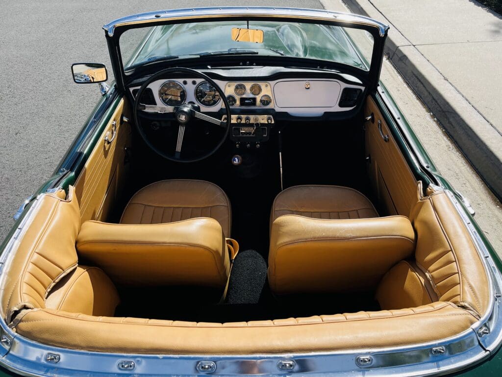 Interior view of a classic convertible car with tan leather seats and vintage dashboard.