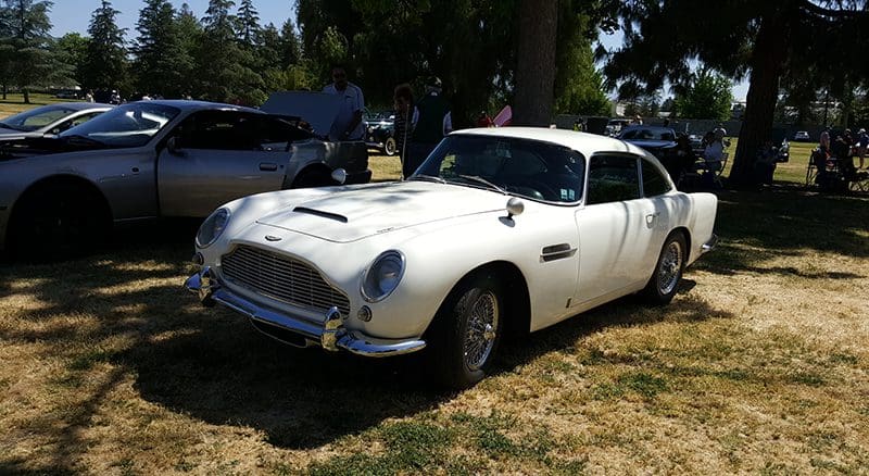 Classic white vintage car parked on grass under trees.