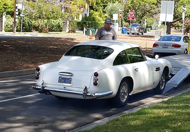 Classic white vintage car parked on a suburban street under trees.
