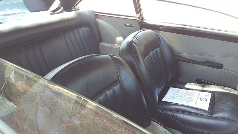 Black leather seats inside a vintage car with a window view.