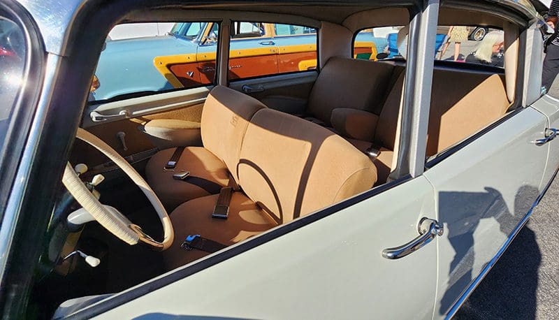 Interior of a classic car with beige seats and a wooden dashboard.