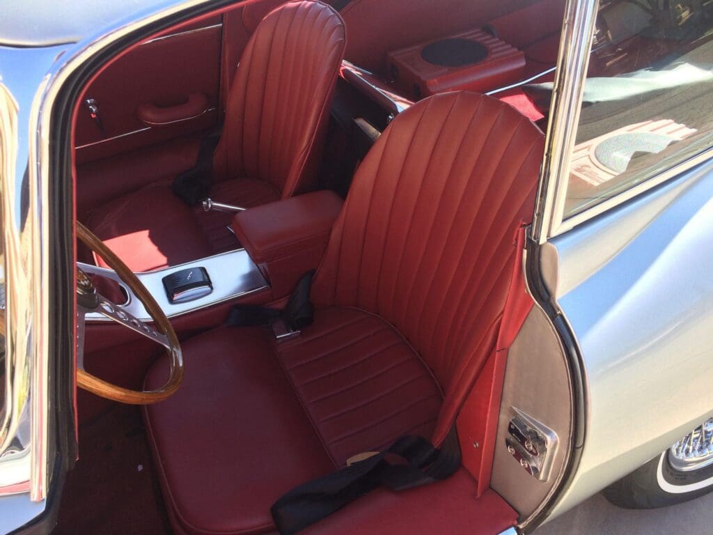 Classic car interior with red leather seats and wooden steering wheel.