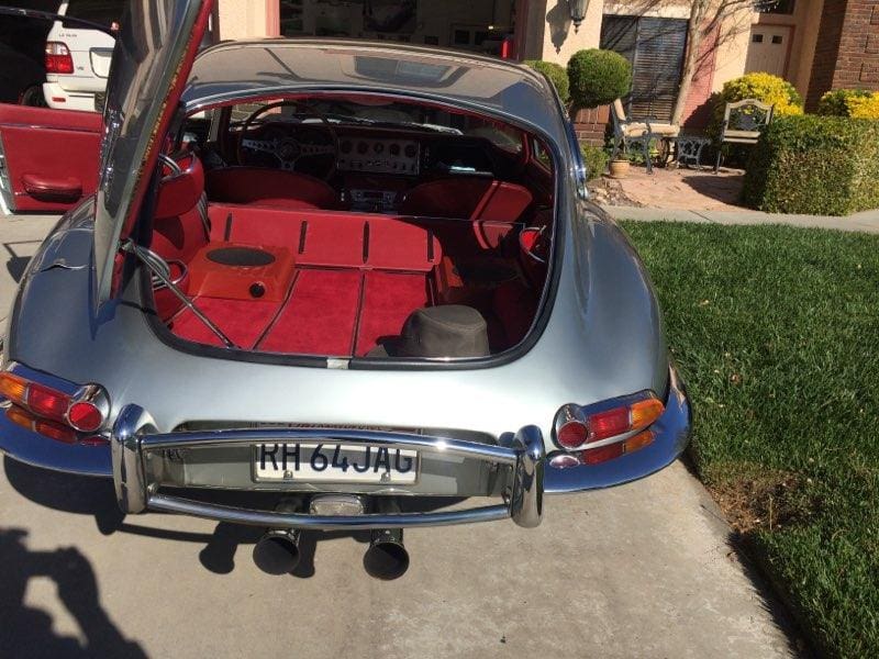 Rear view of a classic silver car with a red interior and hood open.