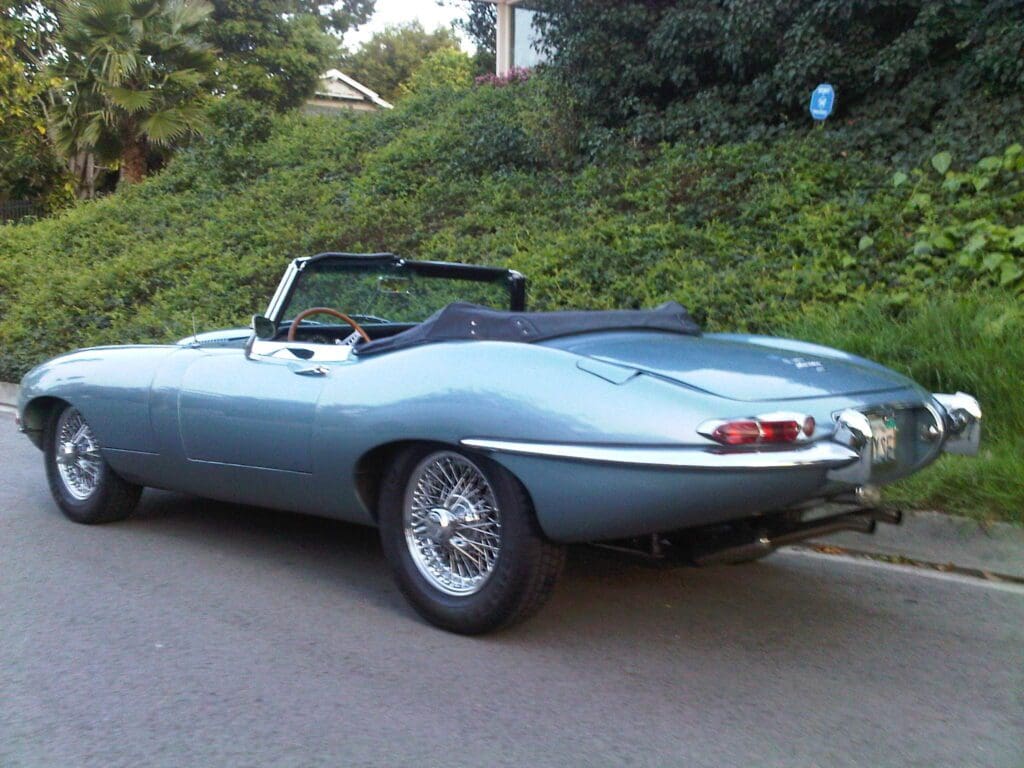 Classic silver convertible sports car parked beside greenery.