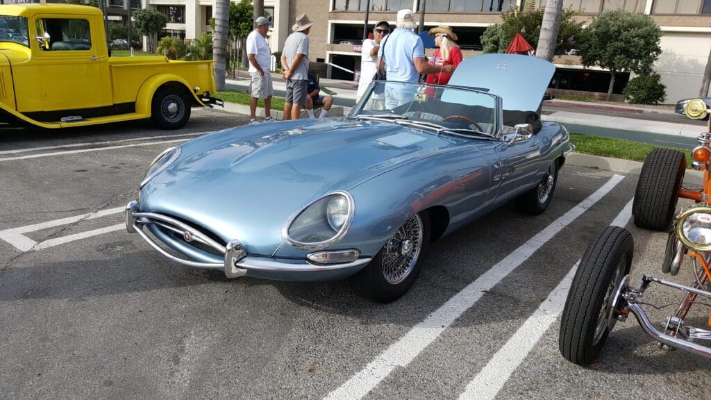 Silver classic Jaguar convertible car parked with hood open at a car show.