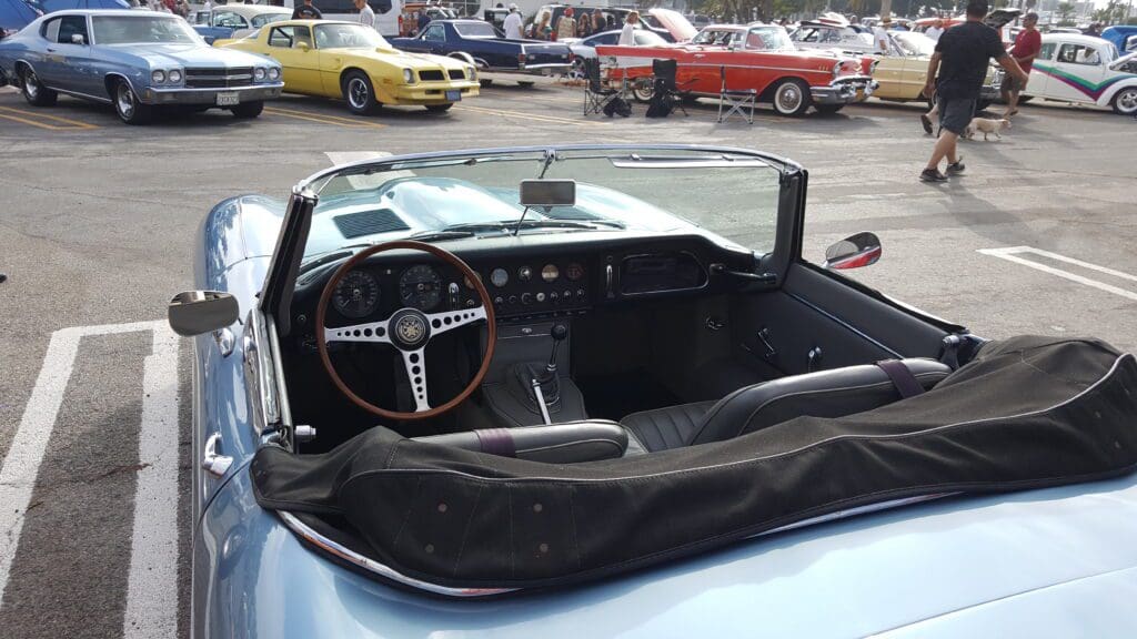 Silver classic Jaguar convertible car parked with hood open at a car show.