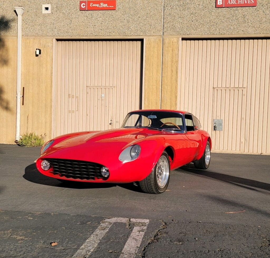 A classic red convertible sports car parked in front of garage doors.