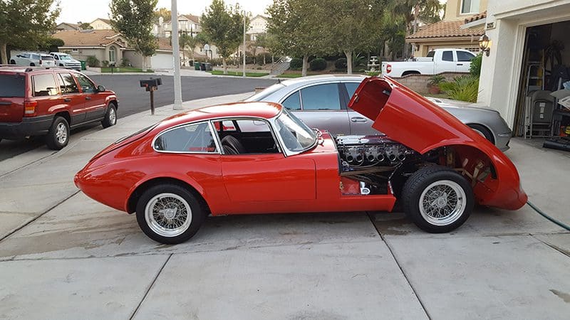 Classic red sports car with its hood open in a driveway.