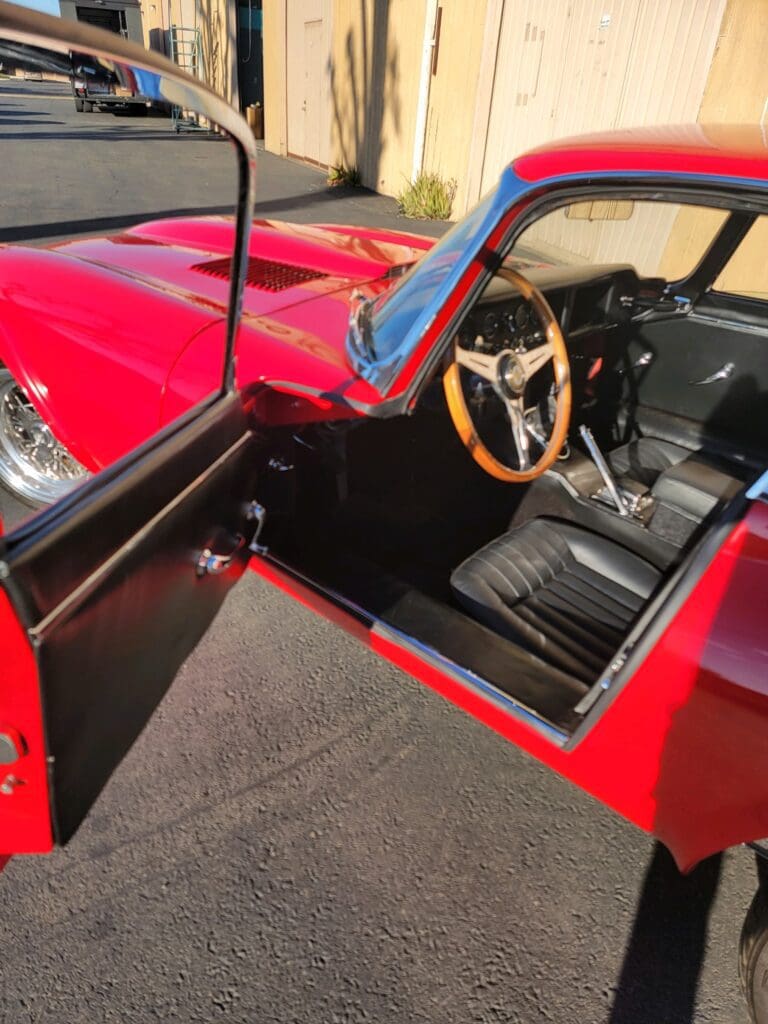 Interior view of a classic red car with black leather seats and wooden steering wheel.