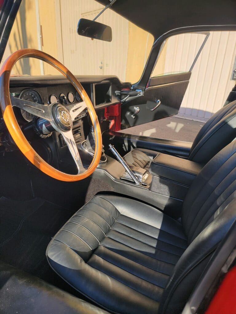 Classic car interior with wooden steering wheel and black leather seats.