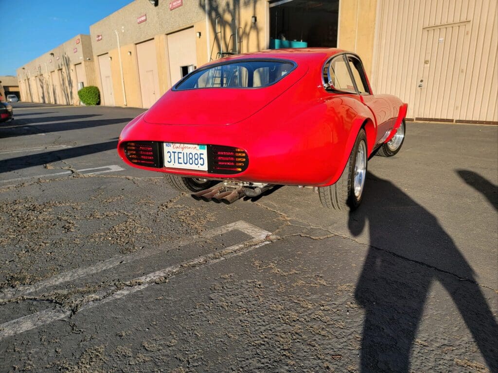 Classic red sports car parked near a beige building on a sunny day.