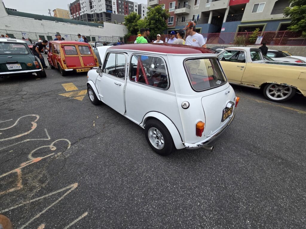 A classic white Mini Cooper parked on a cobblestone street with onlookers around.