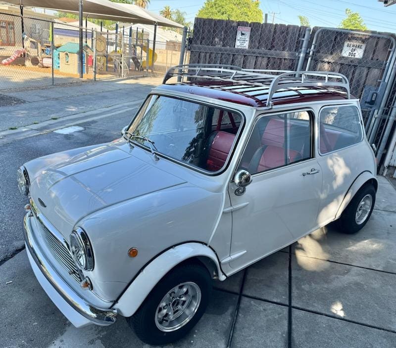 Classic silver Mini Cooper parked outdoors with roof rack under sunny sky.
