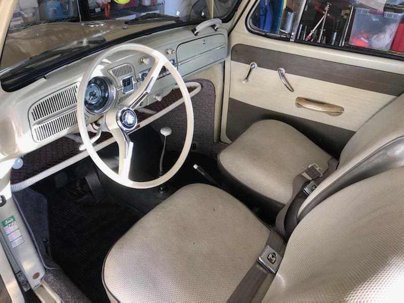 Interior of a vintage car with white steering wheel and beige seats.