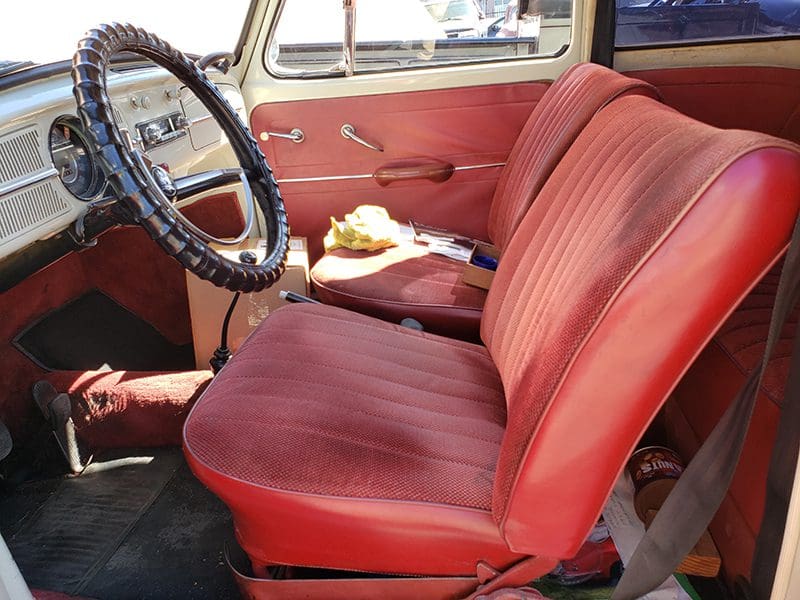 Vintage car interior with red fabric seats and a cat resting on the passenger seat.