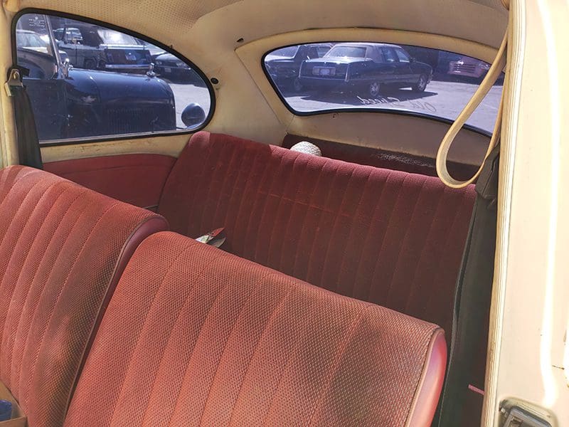 Interior of a vintage car with red fabric seats and rounded windows.