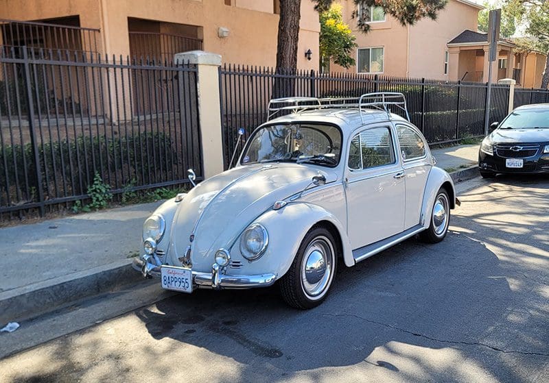 Classic white Volkswagen Beetle parked by the sidewalk.