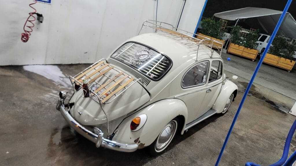 A vintage white Volkswagen Beetle with a wooden roof rack.