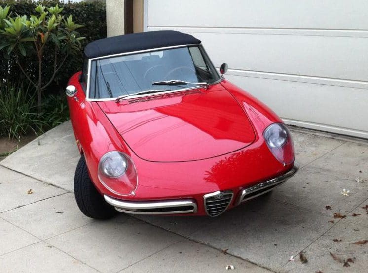 A red classic Alfa Romeo convertible parked outside a garage.