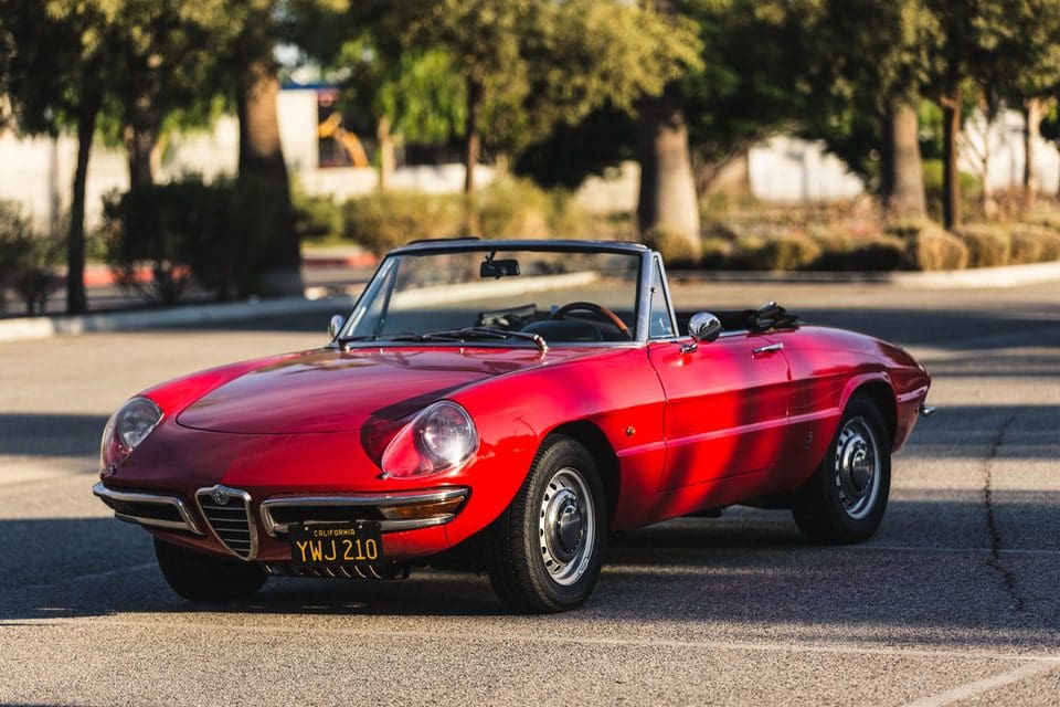 Classic red convertible sports car parked on a sunny street.