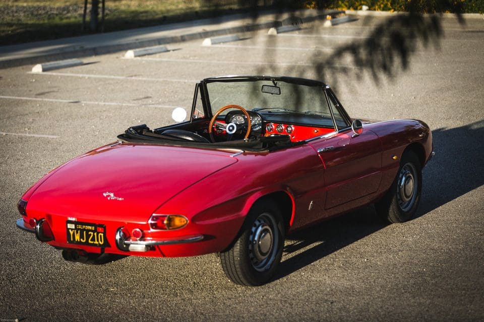 Classic red convertible sports car parked on a sunny road.