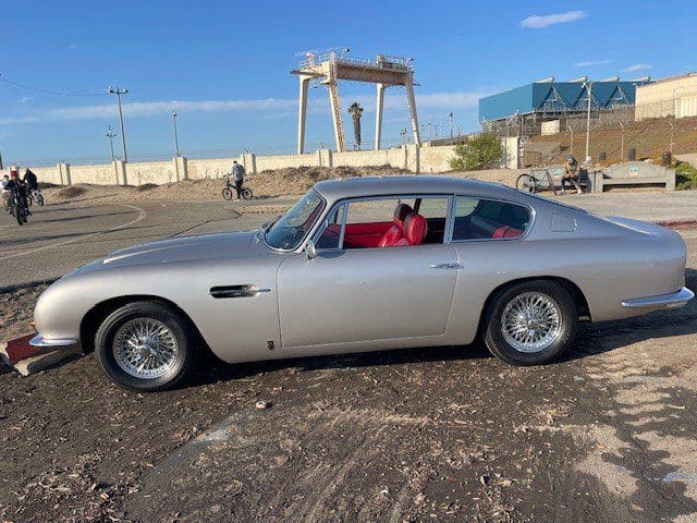 Classic silver sports car with red interior parked outdoors on a sunny day.